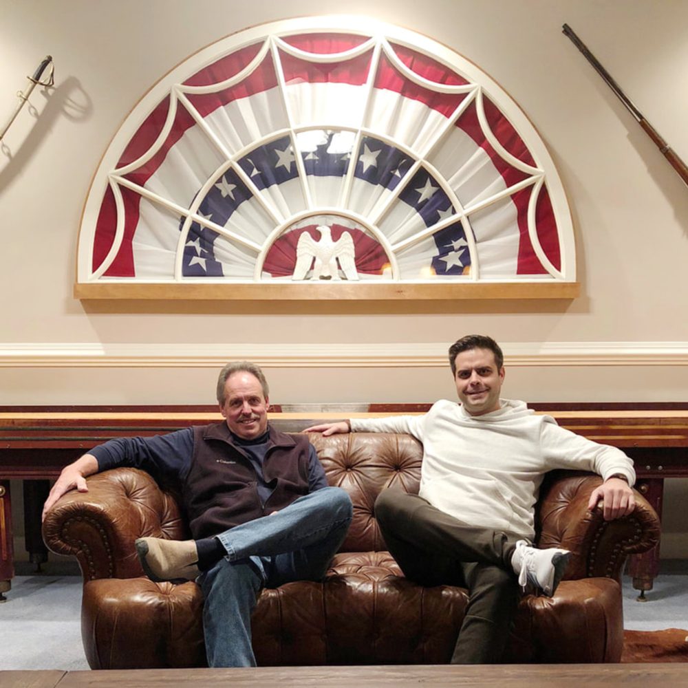 Scott North and his son, Patrick North, seated on a tufted leather sofa